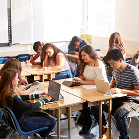 High School Students Sitting At Desks In Classroom Using Laptops